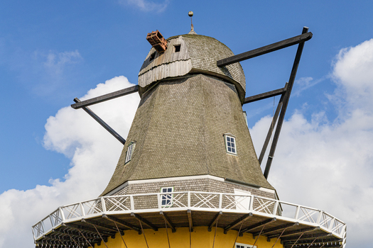 View of the historic windmill on the Hindsholm peninsula with its wooden shingled cap and white gallery railing against a blue sky in Kerteminde Denmark. View of the historic windmill on the Hindsholm peninsula with its wooden shingled cap and white gallery railing against a blue sky in Kerteminde Denmark.