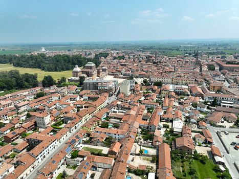 Aerial view of the Royal Palace of Racconigi surrounded by historic red tiled rooftops lush green parkland and the urban layout under a clear blue sky in Racconigi Piemonte Italy.