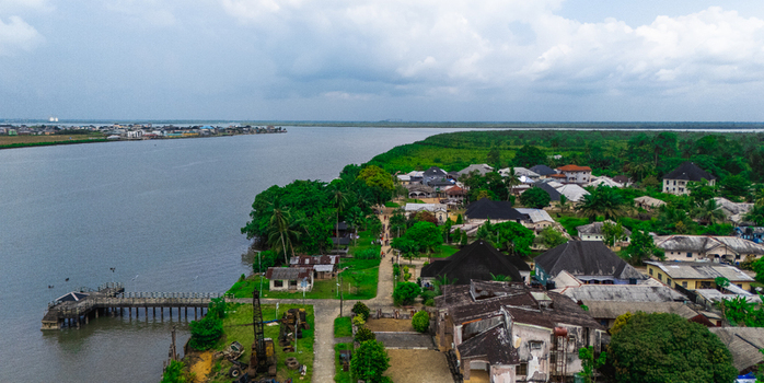 Aerial view of the coastal settlement of Minima with houses nestled among lush trees a wooden pier extending into the river and a cloudy sky in Minima Rivers Nigeria.