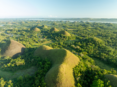 Aerial view of the iconic Chocolate Hills featuring numerous grass covered conical mounds rising above the lush tropical landscape in Batuan Central Visayas Philippines. Aerial view of the iconic Chocolate Hills featuring numerous grass covered conical mounds rising above the lush tropical landscape in Batuan Central Visayas Philippines.