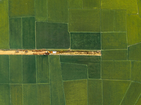 Aerial view of vibrant green rice fields divided by a narrow dirt road with construction machinery working in Lien Son Lak Dak Lak Vietnam. Aerial view of vibrant green rice fields divided by a narrow dirt road with construction machinery working in Lien Son Lak Dak Lak Vietnam.