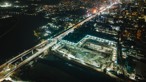Aerial view of a construction site at night featuring illuminated excavation pits surrounding urban infrastructure and light trails from traffic on nearby roads in Chennai Tamil Nadu India.