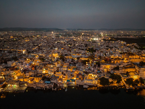 Aerial view of the illuminated city of Udaipur at night featuring historic buildings along the banks of Lake Pichola glowing street lights and a dense urban landscape in Udaipur Rajasthan India.