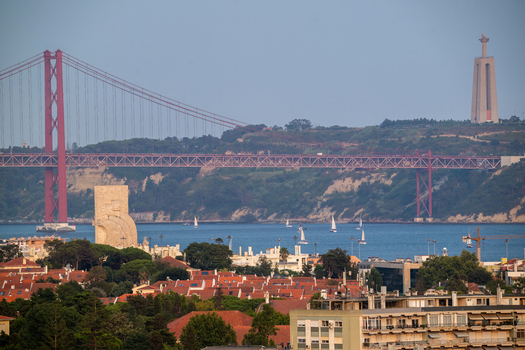 Aerial view of the Padrao dos Descobrimentos and the red 25 de Abril Bridge spanning the Tagus River with the Cristo Rei statue and urban rooftops in Lisboa Lisboa Portugal.