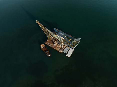 Aerial view of a large industrial floating crane barge and a small boat on the calm dark waters of the Mediterranean Sea near Augusta Sicily Italy. Aerial view of a large industrial floating crane barge and a small boat on the calm dark waters of the Mediterranean Sea near Augusta Sicily Italy.