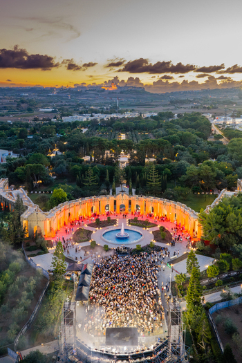 Attard Malta 20 September 2026 Aerial view of a large crowd gathered for an outdoor concert at Park Nazzjonali Ta Qali featuring a central fountain illuminated by warm lights under a sunset sky. Attard Malta 20 September 2026 Aerial view of a large crowd gathered for an outdoor concert at Park Nazzjonali Ta Qali featuring a central fountain illuminated by warm lights under a sunset sky.