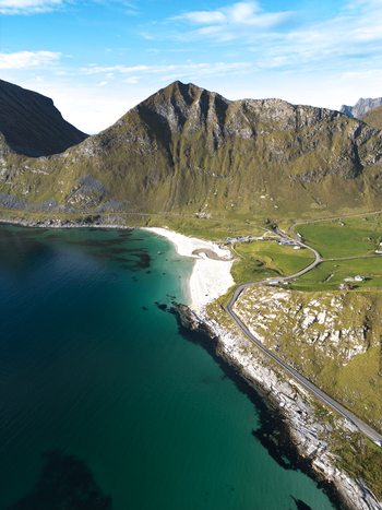 Aerial view of Vik Strand beach with turquoise water steep green mountains and a winding coastal road in Leknes Nordland Norway. Aerial view of Vik Strand beach with turquoise water steep green mountains and a winding coastal road in Leknes Nordland Norway.