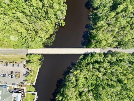 Aerial view of the bridge crossing Sixmile Creek surrounded by dense green forest and dark water in St. Johns County Florida United States.