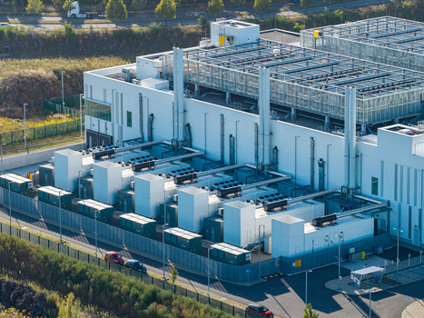 Aerial view of the Vantage Data Centers BER1 facility featuring large white industrial buildings cooling units exhaust stacks and a fenced perimeter in Ludwigsfelde Brandenburg Germany. Aerial view of the Vantage Data Centers BER1 facility featuring large white industrial buildings cooling units exhaust stacks and a fenced perimeter in Ludwigsfelde Brandenburg Germany.
