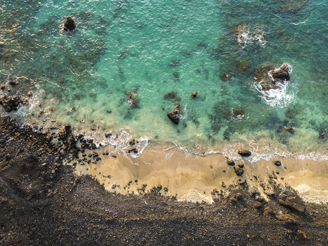 Aerial view of Waikoloa Beach featuring turquoise ocean water dark volcanic rocks and a sandy shoreline with gentle waves in Waikoloa Village Hawaii United States.