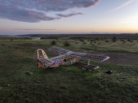 Aerial view of an abandoned graffiti covered biplane resting in a grassy field under a soft sunset sky in Bulgaria. Aerial view of an abandoned graffiti covered biplane resting in a grassy field under a soft sunset sky in Bulgaria.
