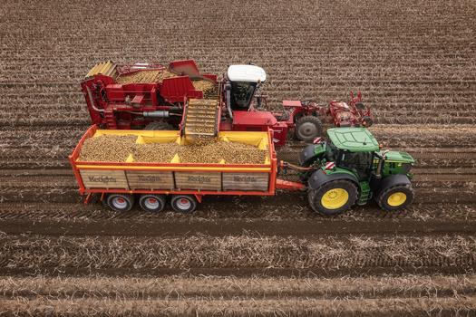 Aerial view of Keogh s Farm potato harvester loading potatoes into a trailer pulled by a green tractor in a brown field Oldtown County Dublin Ireland. Aerial view of Keogh s Farm potato harvester loading potatoes into a trailer pulled by a green tractor in a brown field Oldtown County Dublin Ireland.