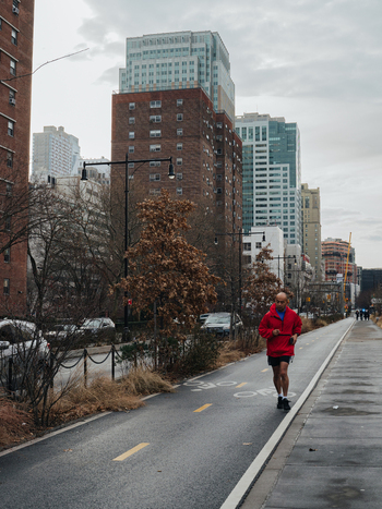 View of a man jogging along a bike path in an urban setting with tall brick buildings and trees in New York New York United States.