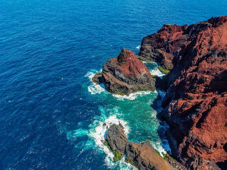 Aerial view of the rugged red volcanic cliffs meet the turquoise ocean as waves crash against the shore Capelo A&ccedil;ores Portugal.