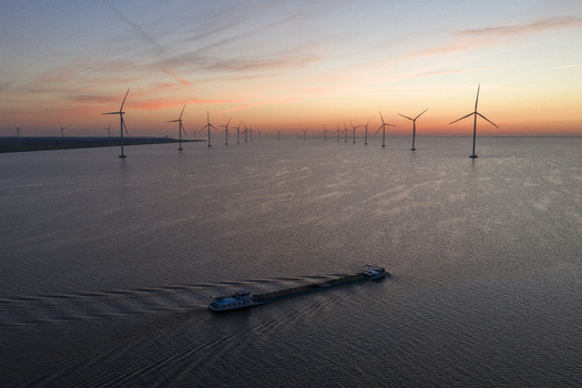 Aerial view of IJsselmeer with offshore wind turbines and a cargo ship at sunset in Netherlands.