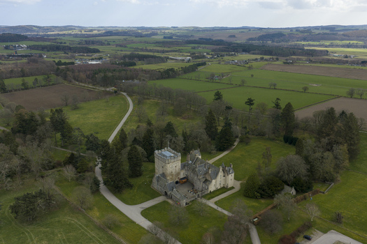 Aerial view of Drum Castle surrounded by lush green lawns tall trees and rolling agricultural fields in Drumoak Scotland United Kingdom.