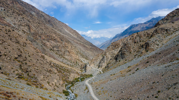 Aerial view of the winding dirt road through the rugged Sadpara Gol valley with a mountain stream and rocky slopes under a blue sky in Skardu Gilgit Pakistan.