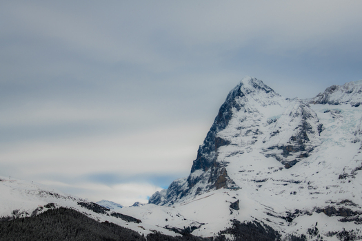 View of a majestic snow covered mountain peak piercing the cloudy sky its rugged texture contrasting with the soft clouds in a serene alpine landscape Murren Switzerland. View of a majestic snow covered mountain peak piercing the cloudy sky its rugged texture contrasting with the soft clouds in a serene alpine landscape Murren Switzerland.