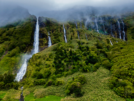Aerial view of multiple waterfalls cascading down a lush green mountainside shrouded in mist creating a serene and ethereal landscape Flores Azores Portugal.