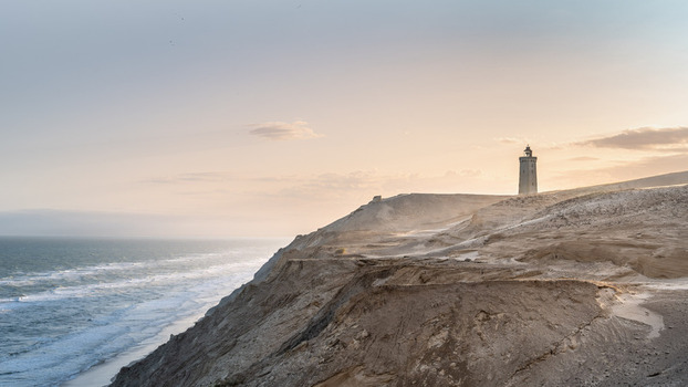 View of Rubjerg Knude lighthouse standing on the sandy cliffs overlooking the North Sea at sunset in Lokken Denmark. View of Rubjerg Knude lighthouse standing on the sandy cliffs overlooking the North Sea at sunset in Lokken Denmark.