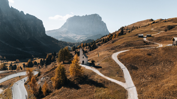 Aerial view of Cappella di San Maurizio nestled among golden autumn larches with the majestic Dolomites and winding mountain roads in Selva di Val Gardena Trentino Alto Adige Italy. Aerial view of Cappella di San Maurizio nestled among golden autumn larches with the majestic Dolomites and winding mountain roads in Selva di Val Gardena Trentino Alto Adige Italy.