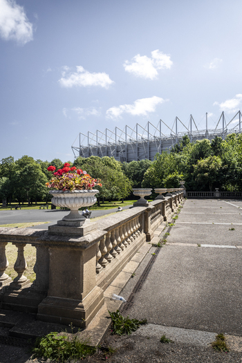 View of St James Park stadium seen from a stone balustrade with a decorative flower pot in the foreground located in a park in Newcastle upon Tyne England United Kingdom. View of St James Park stadium seen from a stone balustrade with a decorative flower pot in the foreground located in a park in Newcastle upon Tyne England United Kingdom.