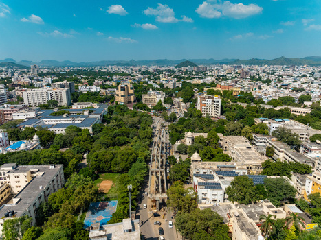 Aerial view of the urban landscape of Udaipur with lush green trees residential buildings and a central road construction project in Udaipur Rajasthan India.