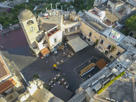 Aerial view of the historic Piazzetta square with its yellow clock tower people walking and white cafe umbrellas in Capri Campania Italy.