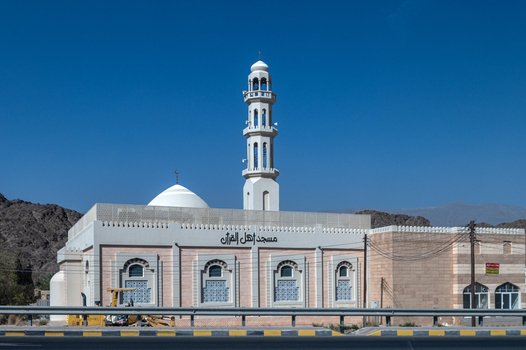 View of the Ahl Al Quran Mosque with its white dome and tall minaret set against a clear blue sky and rugged mountains in Muscat Muscat Governorate Oman. View of the Ahl Al Quran Mosque with its white dome and tall minaret set against a clear blue sky and rugged mountains in Muscat Muscat Governorate Oman.