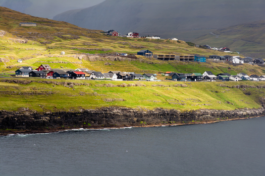 View of a coastal village with colorful houses nestled on a green hillside overlooking the sea in the Faroe Islands.