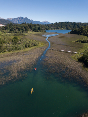 Aerial view of kayakers paddling through a narrow channel in Nahuel Huapi Lake surrounded by dense forests and majestic mountains San Carlos de Bariloche Rio Negro Argentina. Aerial view of kayakers paddling through a narrow channel in Nahuel Huapi Lake surrounded by dense forests and majestic mountains San Carlos de Bariloche Rio Negro Argentina.
