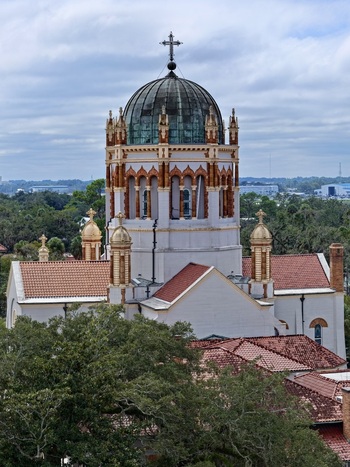 Aerial view of the ornate copper dome and red tile roofs of the historic Memorial Presbyterian Church surrounded by lush trees in St. Augustine Florida United States.