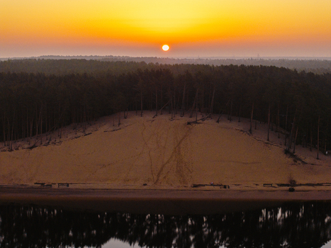 Aerial view of Lielupe White Dune at sunrise with pine trees atop the sandy slope and calm water reflecting the golden light in Jurmala Latvia. Aerial view of Lielupe White Dune at sunrise with pine trees atop the sandy slope and calm water reflecting the golden light in Jurmala Latvia.