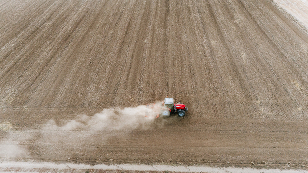 Aerial view of a red tractor plowing a large brown field creating a cloud of dust behind it in Veliki Radinci Vojvodina Serbia. Aerial view of a red tractor plowing a large brown field creating a cloud of dust behind it in Veliki Radinci Vojvodina Serbia.