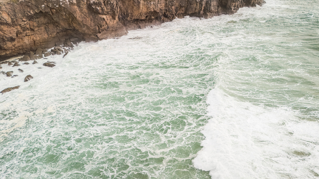 Aerial view of rough turquoise sea waves crashing against the steep rocky cliffs of Sagres with white foam and spray Sagres Faro Portugal. Aerial view of rough turquoise sea waves crashing against the steep rocky cliffs of Sagres with white foam and spray Sagres Faro Portugal.