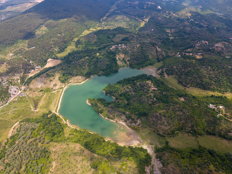 Aerial view of a turquoise lake and reservoir nestled among lush green hills and dense forests under a bright sky in Kruje Durres County Albania.