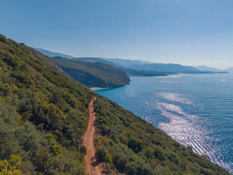Aerial view of Gjipe Beach featuring a rugged dirt path winding along the lush green cliffside overlooking the sparkling blue Ionian Sea in Vlore County Albania. Aerial view of Gjipe Beach featuring a rugged dirt path winding along the lush green cliffside overlooking the sparkling blue Ionian Sea in Vlore County Albania.