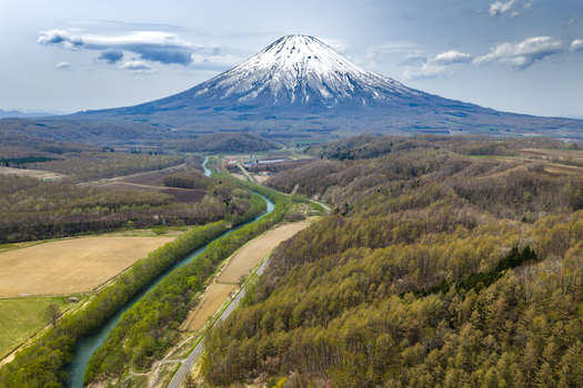 Aerial view of Mount Yotei with its snow capped peak rising above the winding river agricultural fields and lush forests in Niseko Hokkaido Japan.