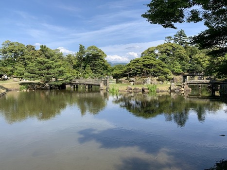 Japan 06 July 2026 View of a traditional Japanese garden with a tranquil pond wooden bridges manicured pine trees and lush greenery under a clear blue sky. Japan 06 July 2026 View of a traditional Japanese garden with a tranquil pond wooden bridges manicured pine trees and lush greenery under a clear blue sky.