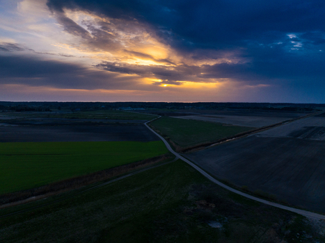 Aerial view of agricultural fields and a rural road at sunset with dramatic clouds and golden light in Skatre South Kurzeme Municipality Latvia. Aerial view of agricultural fields and a rural road at sunset with dramatic clouds and golden light in Skatre South Kurzeme Municipality Latvia.
