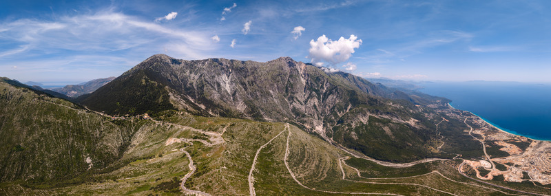Aerial view of winding mountain roads and rugged peaks overlooking the turquoise coastline under a clear blue sky in Palase Vlore County Albania.