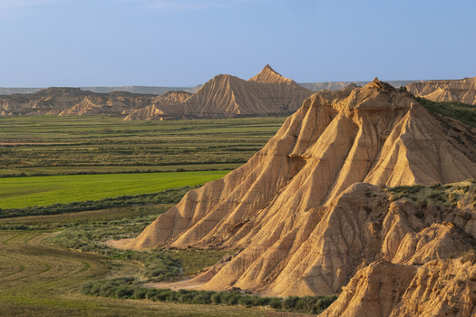 View of the unique sandstone rock formations and arid badlands of Bardenas Reales with green fields in the foreground in Navarre Navarre Spain. View of the unique sandstone rock formations and arid badlands of Bardenas Reales with green fields in the foreground in Navarre Navarre Spain.