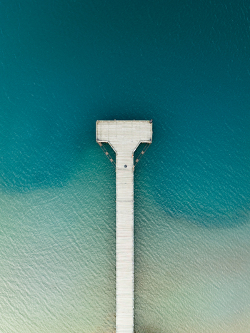 Aerial view of a stark white pier stretching into the turquoise depths of the lake a beacon of contrast against the shimmering waters Glenorchy Otago Region New Zealand. Aerial view of a stark white pier stretching into the turquoise depths of the lake a beacon of contrast against the shimmering waters Glenorchy Otago Region New Zealand.