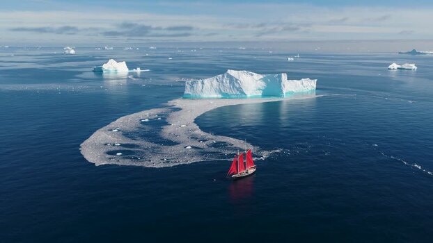 Aerial view of red sailed ship near iceberg in Greenland. Aerial view of red sailed ship near iceberg in Greenland.