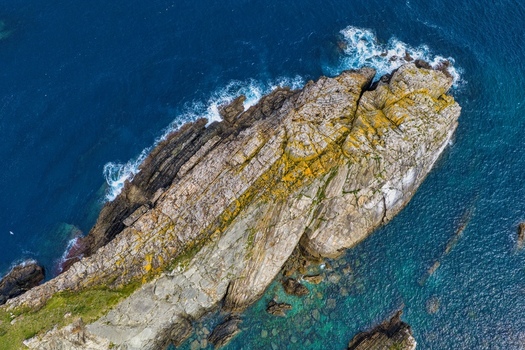 Aerial view of Silence Beach Viewpoint with jagged rocky cliffs and white waves crashing against the shore in Cudillero Asturias Spain.