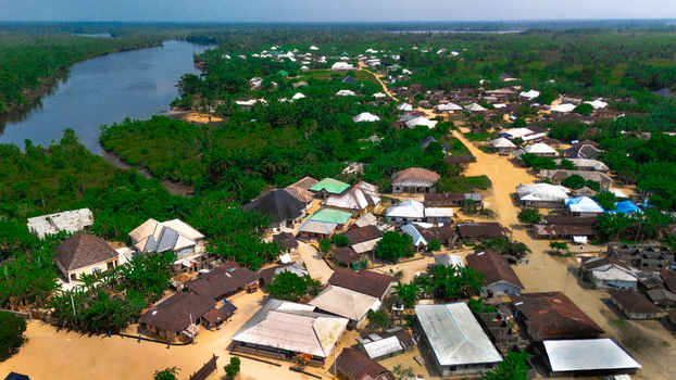 Aerial view of a rural village nestled along a winding river featuring traditional houses with metal roofs lush tropical vegetation and dirt paths in Abua Rivers Nigeria. Aerial view of a rural village nestled along a winding river featuring traditional houses with metal roofs lush tropical vegetation and dirt paths in Abua Rivers Nigeria.