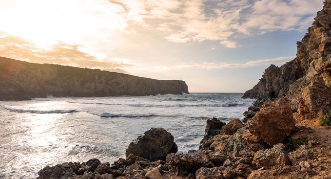 View of Spiaggia di Cala Domestica with waves crashing against the rocky cliffs under a golden sunset sky Provincia del Sulcis Iglesiente Sardegna Italy. View of Spiaggia di Cala Domestica with waves crashing against the rocky cliffs under a golden sunset sky Provincia del Sulcis Iglesiente Sardegna Italy.