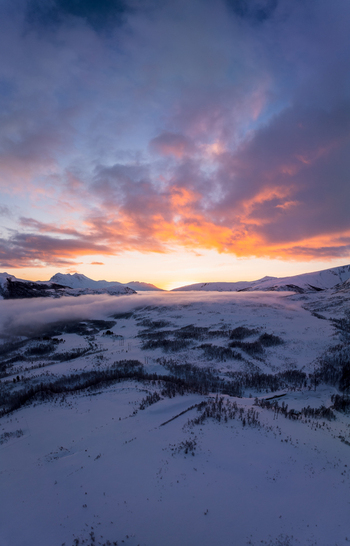 Aerial view of the winter landscape on Kvaloya island with snow covered terrain low hanging clouds and a vibrant sunset sky in Troms Norway.