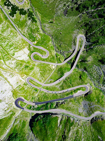 Aerial view of the winding Transfagarasan road with sharp hairpin turns cutting through the lush green mountain landscape in Curtea de Arges Judetul Arges Romania. Aerial view of the winding Transfagarasan road with sharp hairpin turns cutting through the lush green mountain landscape in Curtea de Arges Judetul Arges Romania.