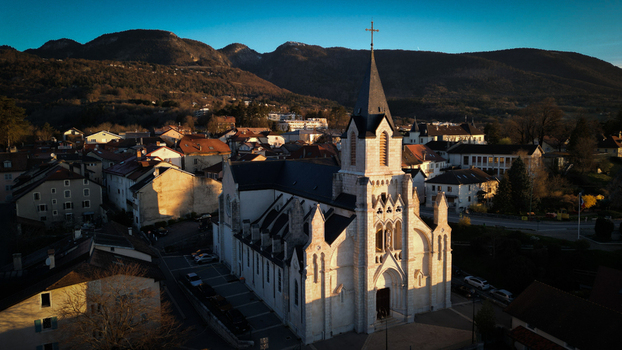 Aerial view of the Eglise Saint Pierre with its tall spire and stone facade surrounded by rooftops and the Jura mountains at sunset in Gex Auvergne Rhone Alpes France. Aerial view of the Eglise Saint Pierre with its tall spire and stone facade surrounded by rooftops and the Jura mountains at sunset in Gex Auvergne Rhone Alpes France.